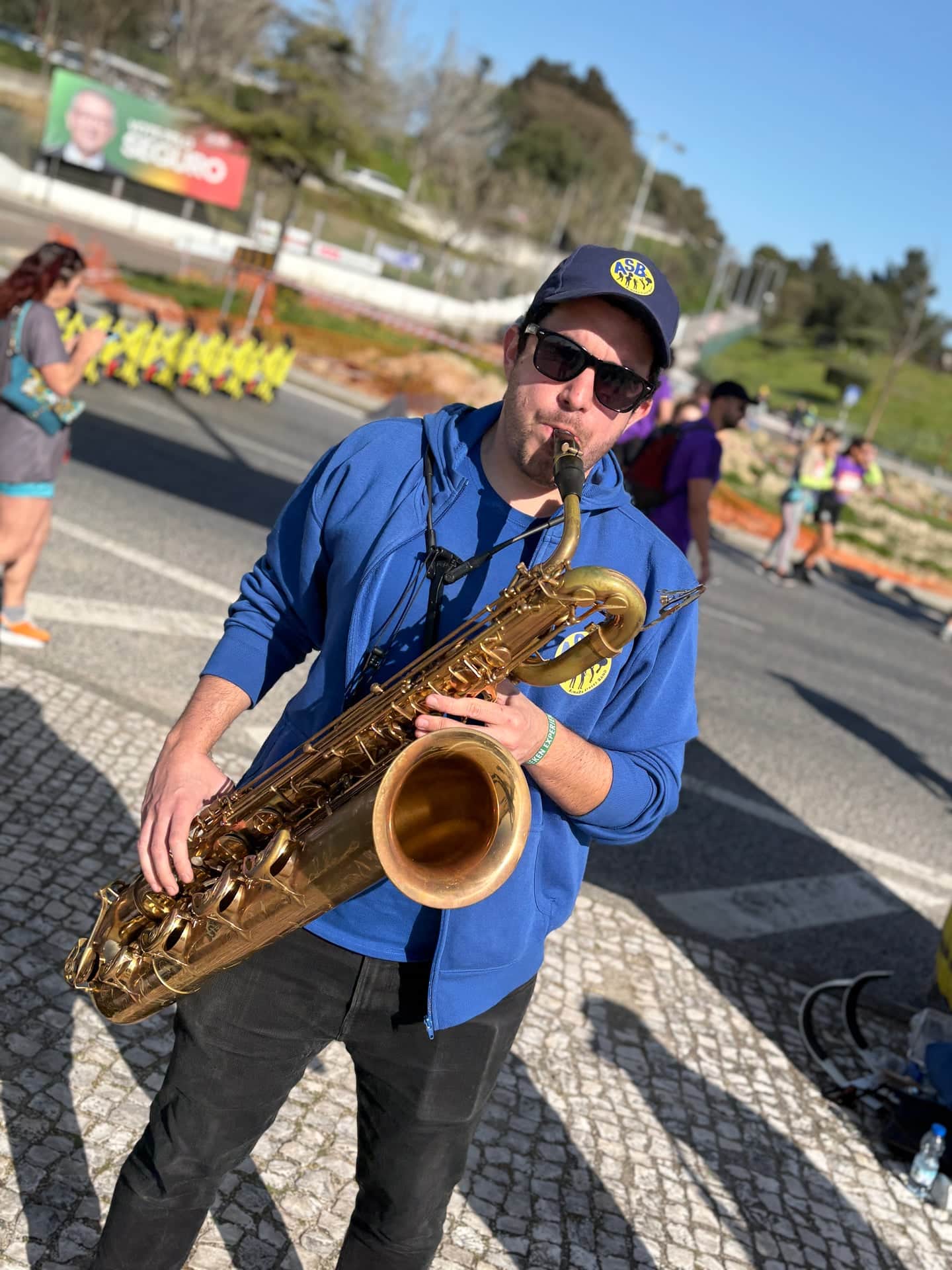 Saxofonista barítono de casaco azul a tocar na calçada