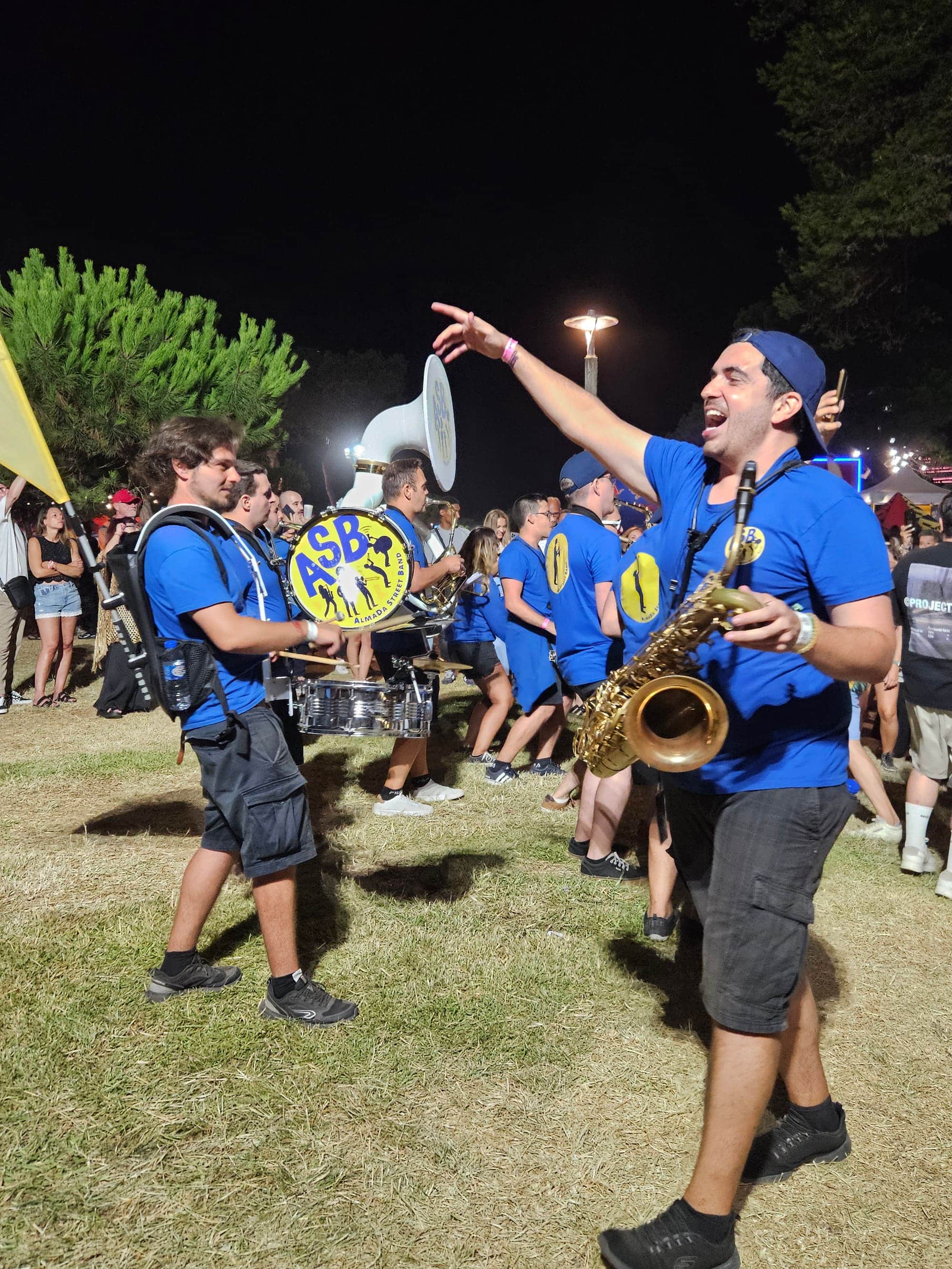 De noite, um músico aponta para a multidão enquanto grita ao megafone, com a banda atrás