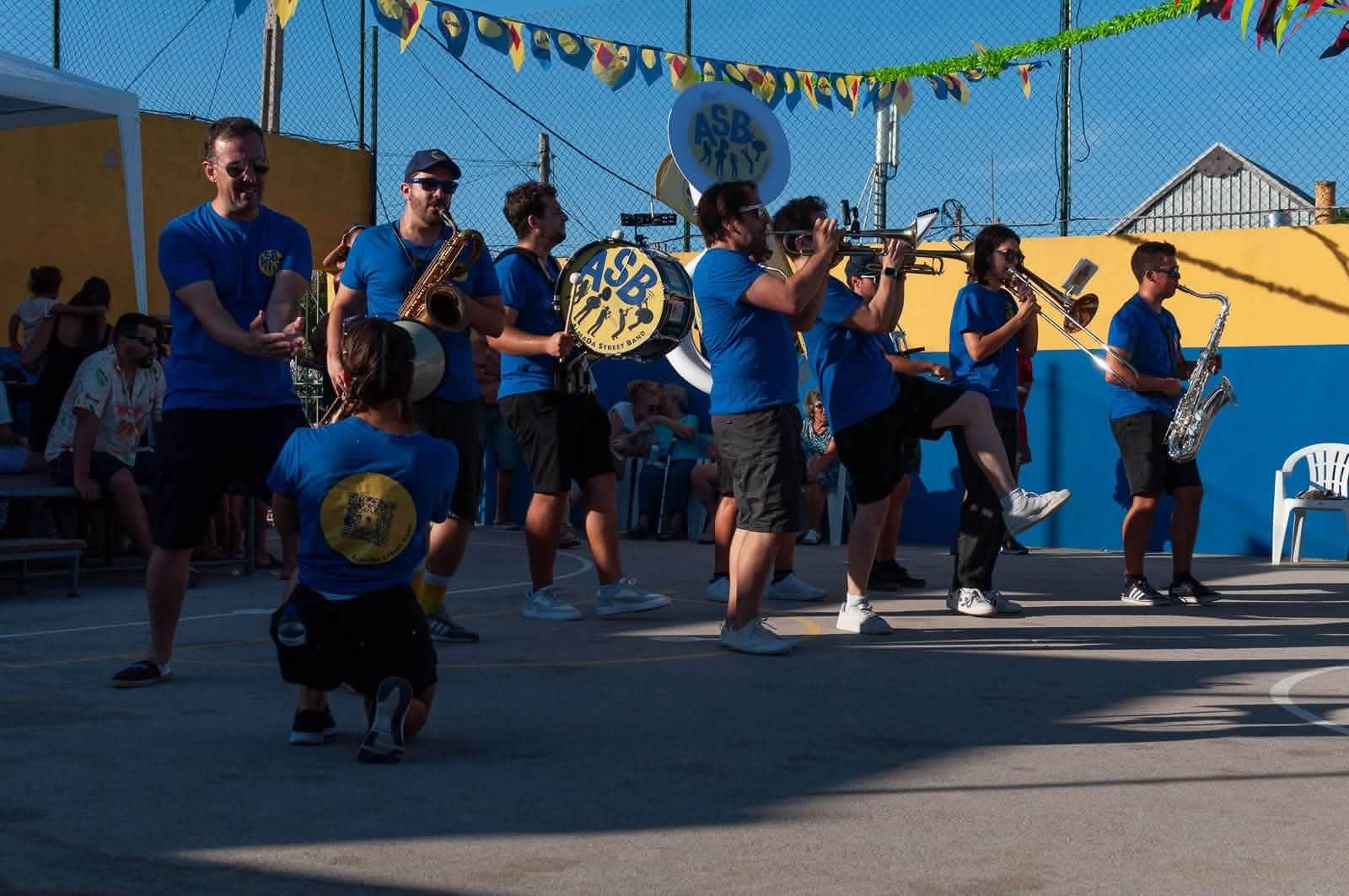 A banda a tocar numa rua enfeitada com bandeirinhas de arraial